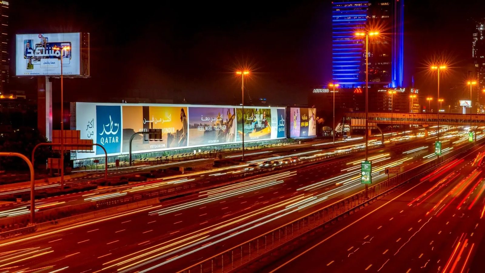 Large Qatar hoarding billboard displaying tourism advertisement on Dubai highway at night