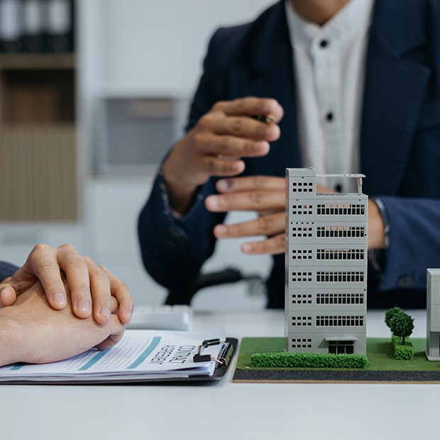 Real estate agent showing architectural building model to client during contract signing