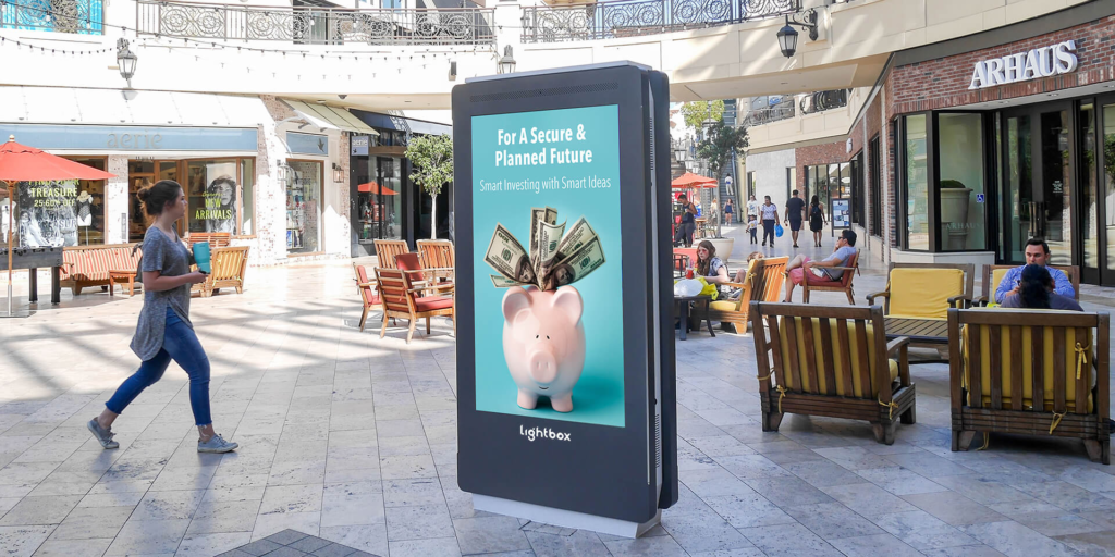 Lightbox digital kiosk screen displaying financial ad in outdoor shopping mall plaza